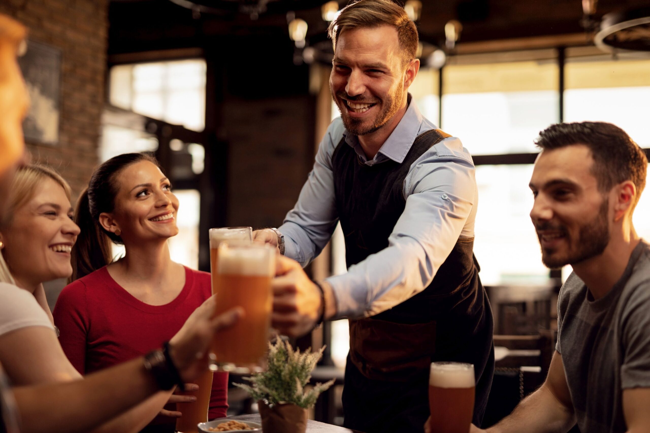 Happy waiter serving beer to group of young people in a pub.