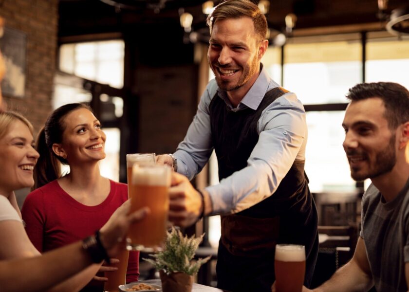 Happy waiter serving beer to group of young people in a pub.