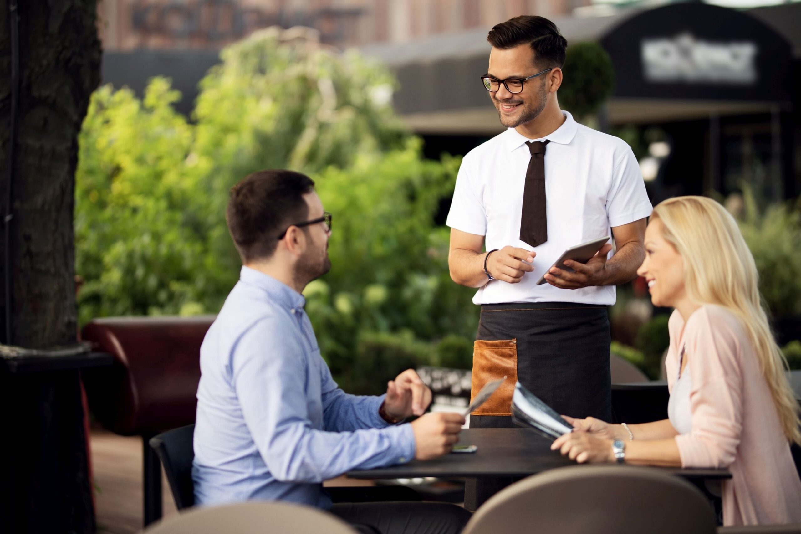 Young smiling waiter talking to a couple while taking their order in a cafe.