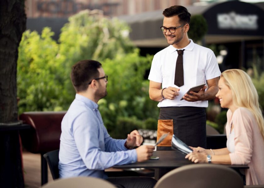 Young smiling waiter talking to a couple while taking their order in a cafe.