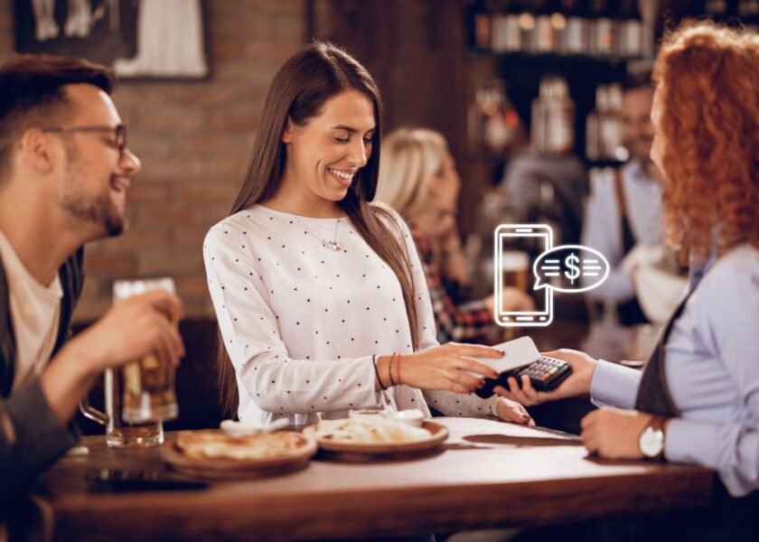 Happy woman making contactless payment to a waitress in a bar.